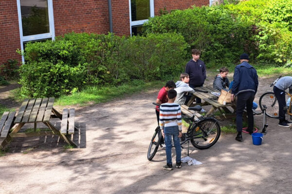 Eine Gruppe von Schülerinnen und Schülern repariert Fahrräder auf dem Schulhof